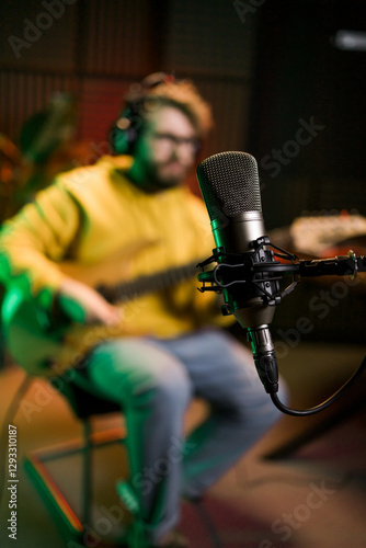 Male singer recording songs by using a studio microphone and and playing guitar in a music recording studio. Performance and show in the music business, streaming and recording music.