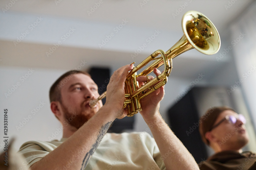 Obraz premium Close up of red haired man playing trumpet enthusiastically while sitting on couch at home with friends, copy space