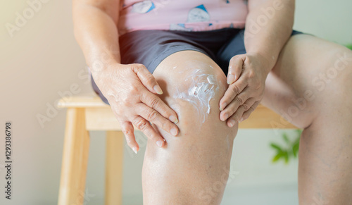 Elderly woman applying cream to knee pain in livingroom, Self-Treatment