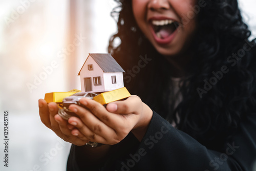 Joyful woman holds miniature house model, car, and gold bars, symbolizing financial success, wealth, and asset ownership. financial success, wealth, asset ownership, investment, financial freedom.