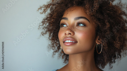 A young woman with radiant skin and a hopeful gaze, her vibrant, curly hair framing her face perfectly, bathed in soft, natural light against a neutral backdrop.