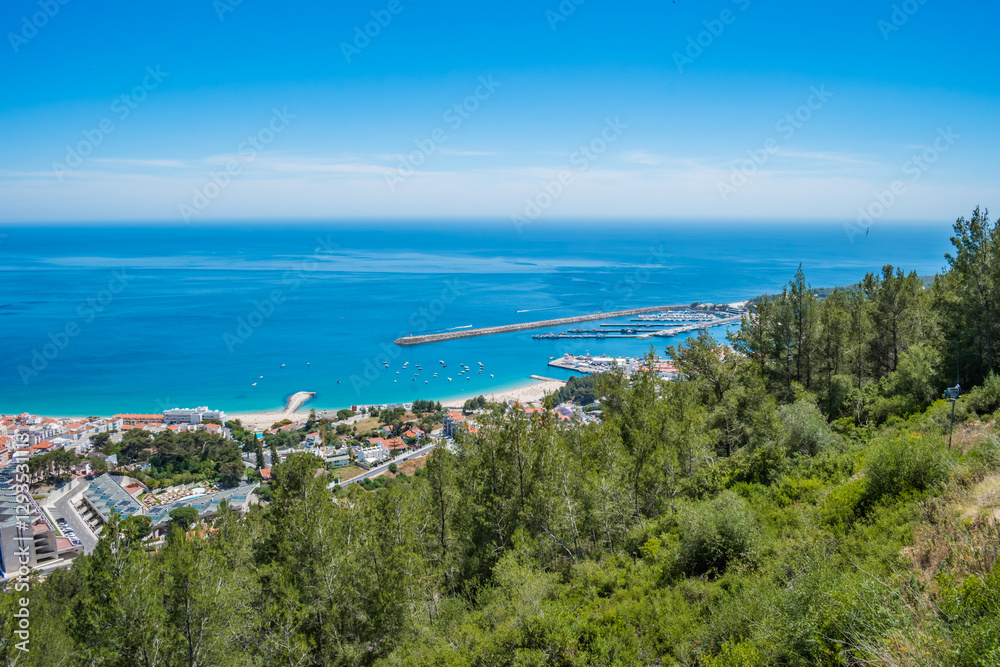 Green forest of the Arrábida natural park with construction of the village of Sesimbra next to the beach and marina in the background, PORTUGAL Green forest of the Arrábida natural park with construction of the village of Sesimbra next to the beach and marina in the background, PORTUGAL