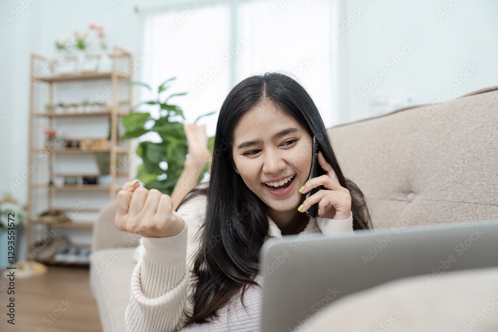 Young woman working from home, smiling and talking on phone while using laptop, expressing excitement. Young woman working from home, smiling and talking on phone while using laptop, expressing excitement.