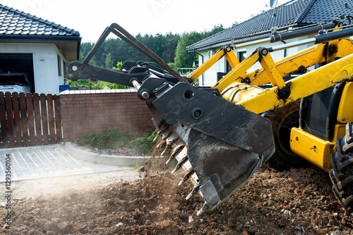 A backhoe loader carries and levels rubble on a dirt road.
