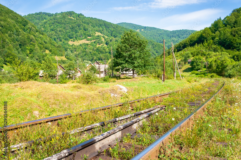 old railroad passes through the valley. mountainous countryside in morning light. sunny weather with blue sky and clouds. trip to alpine village