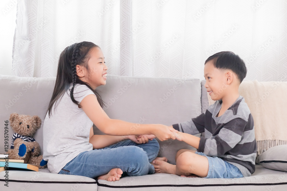 Asian brother and sister sitting on sofa holding hands and laughing together. Playful sibling moment, showing strong bond and joyful expression. Cozy living room setting with relaxed. Asian brother and sister sitting on sofa holding hands and laughing together. Playful sibling moment, showing strong bond and joyful expression. Cozy living room setting with relaxed.