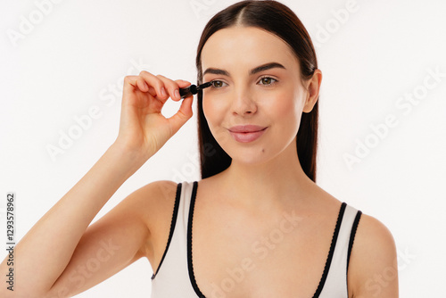 Closeup of a person holding a brush while applying mascara to the eyelashes, smiling gently.