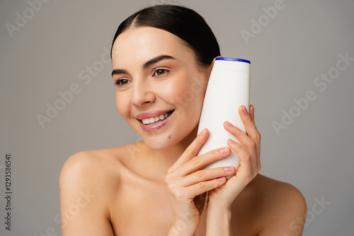 A cheerful individual beautiful female model girl displaying a shampoo bottle, symbolizing personal care and hygiene essentials.