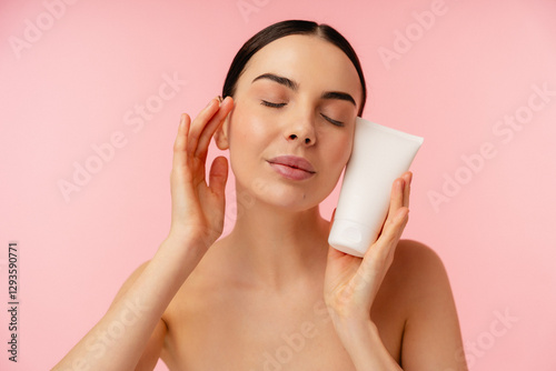Person enjoying skincare routine with a tube of cream against a vibrant pink background.