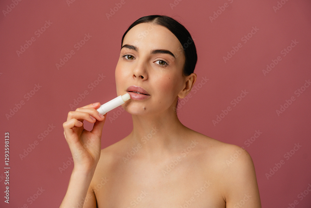 Person applying lip balm against a soft pink background, promoting skincare and beauty concepts. Person applying lip balm against a soft pink background, promoting skincare and beauty concepts.