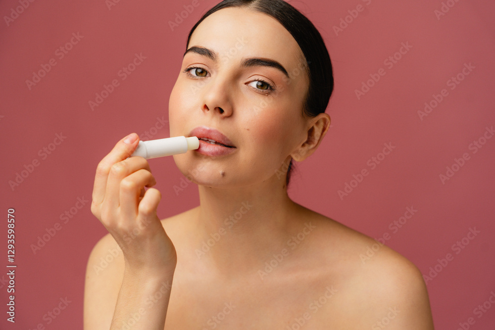 Close-up of an individual applying lip balm, demonstrating skincare and self-care routines against a pink studio background. Close-up of an individual applying lip balm, demonstrating skincare and self-care routines against a pink studio background.