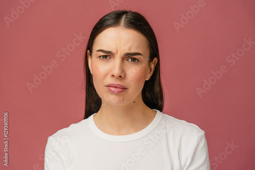 Portrait of a person girl expressing concern or confusion against a plain pink backdrop.