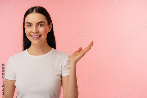 Person in a white casual shirt smiling and gesturing a presentation over a light pink backdrop.
