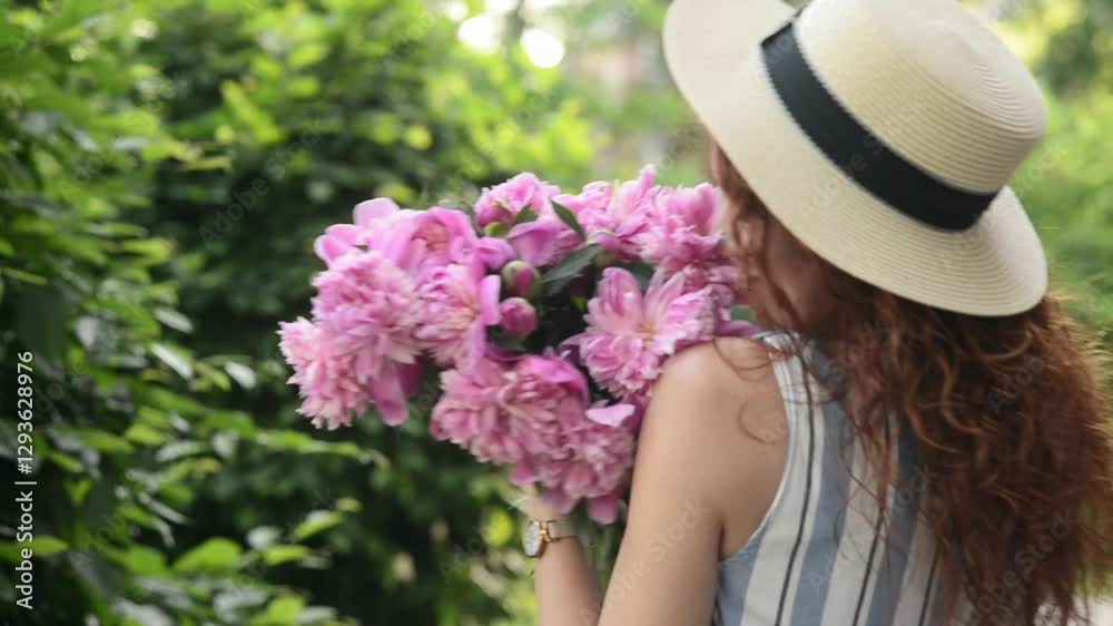 A girl in a summer sundress hat with a basket inhales the scent of flowers, listens to birds singing and holds a bouquet of pink peonies, a peaceful scene, lightness and carelessness. Perfumery, sprin