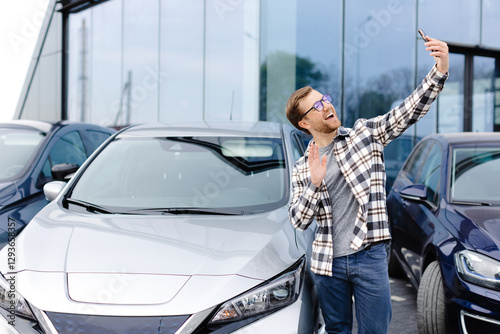 Happy man taking selfie through smart phone after purchasing new car. The man showing the purchased car via video link over the phone