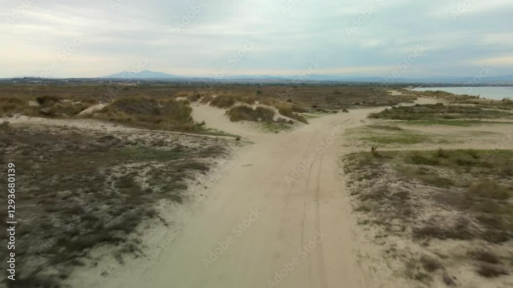 Day view low flight over an empty dirt road and an expansive desert landscape with sandy paths next to the sea under a cloudy sky in Greece. Day view low flight over an empty dirt road and an expansive desert landscape with sandy paths next to the sea under a cloudy sky in Greece.