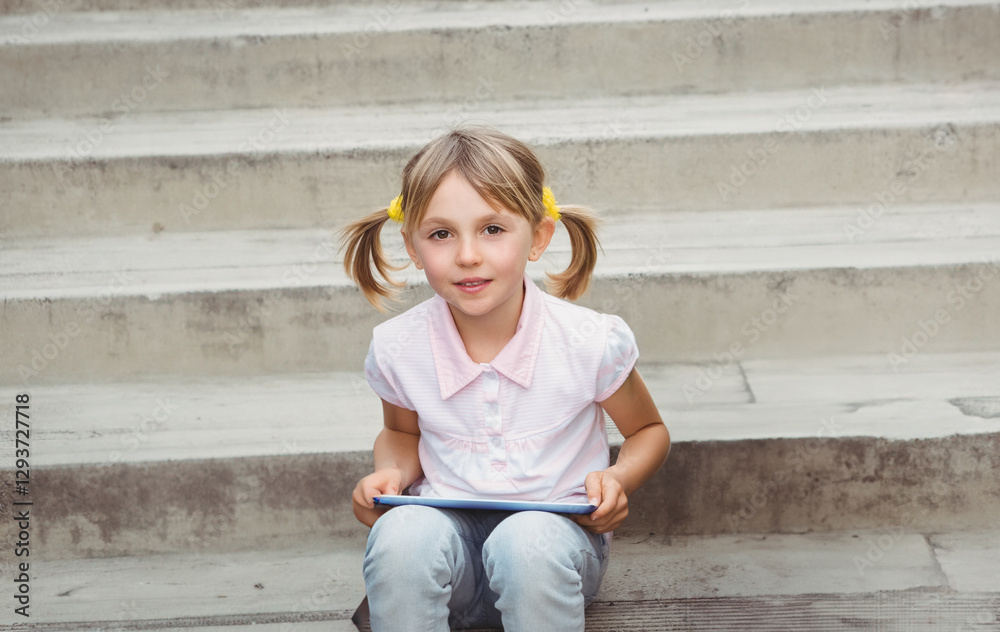 Sitting on steps outdoors, child holding tablet and smiling brightly Sitting on steps outdoors, child holding tablet and smiling brightly