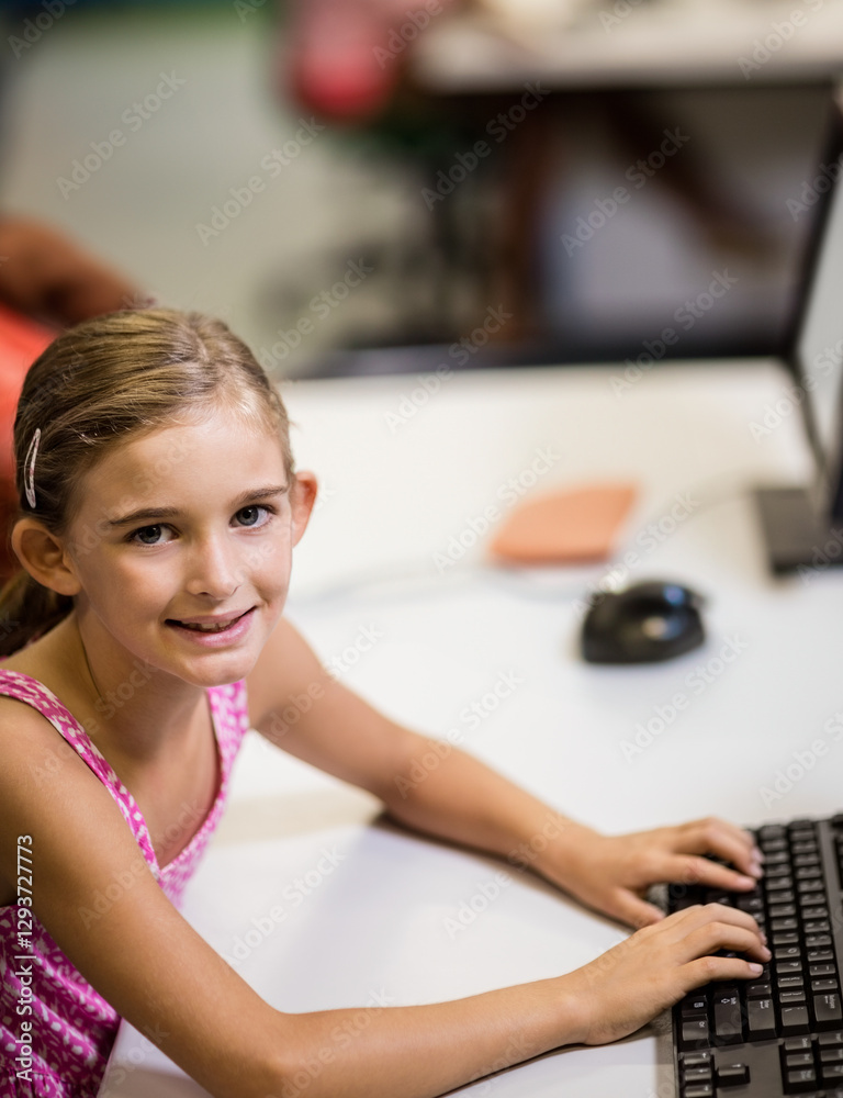 Smiling girl using computer in school classroom, engaging in digital learning
