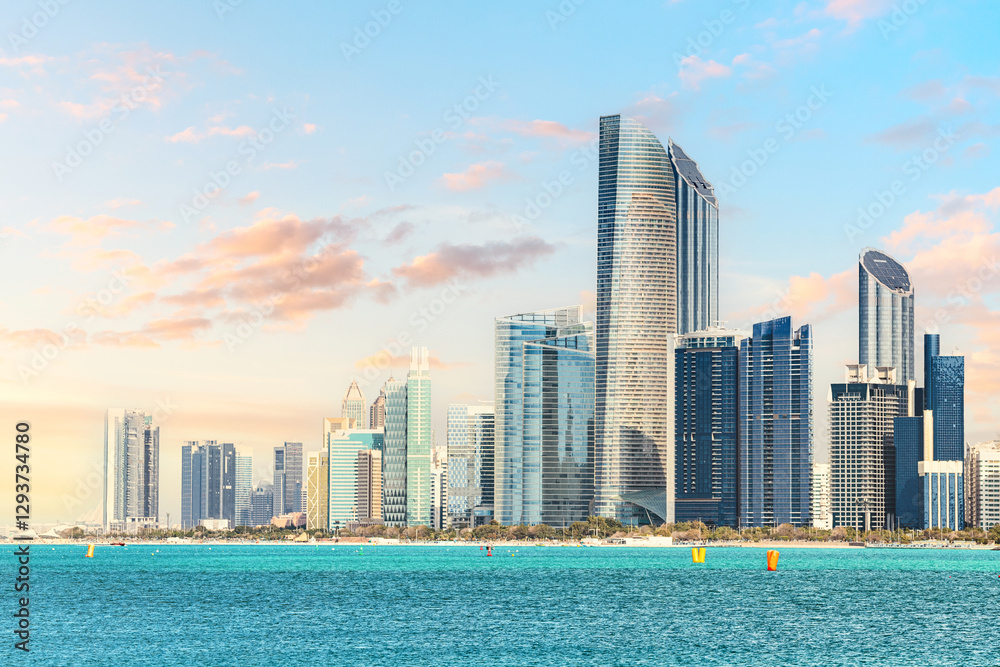 Fototapeta premium Modern skyscrapers reflecting on turquoise sea at sunset in Abu Dhabi, United Arab Emirates