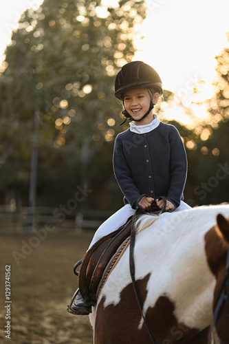 A young girl rider in a helmet and equestrian boots sits on her beloved horse at the stable, enjoying a peaceful horseback ride.