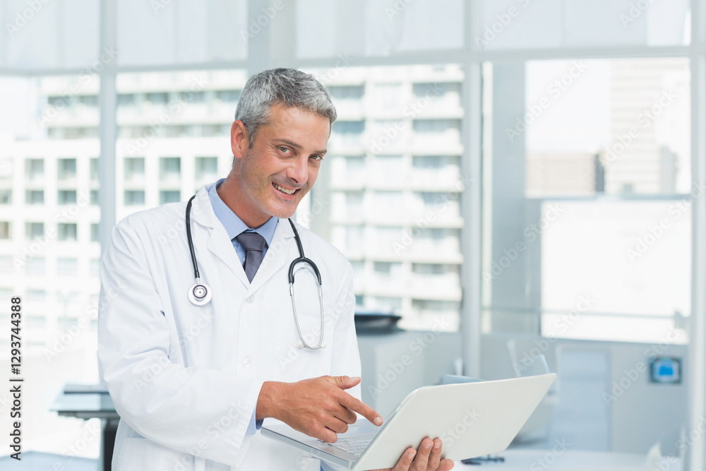 Doctor in office smiling while using laptop for medical research Doctor in office smiling while using laptop for medical research