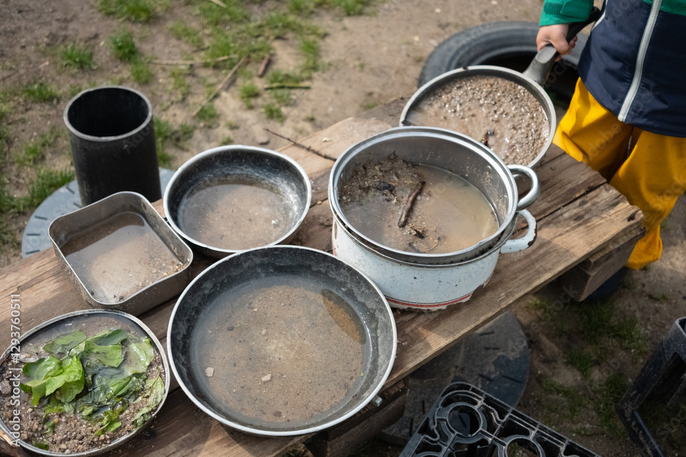 A lively mud kitchen in a kindergarten where children engage in free play, using pots, pans, and plates filled with sand, water, mud, and leaves. Montessori-inspired hands-on learning. A lively mud kitchen in a kindergarten where children engage in free play, using pots, pans, and plates filled with sand, water, mud, and leaves. Montessori-inspired hands-on learning.