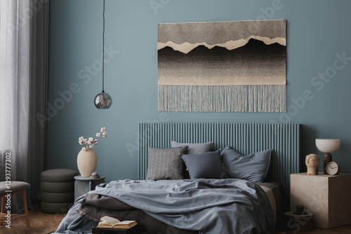 Stylish bedroom with a headboard in soft blue, a decorative woven tapestry, and an inviting bed with layered pillows and blankets. photo