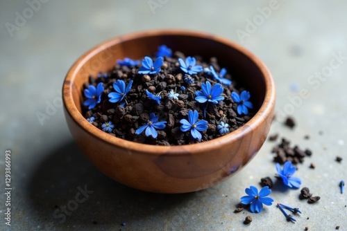 Wooden bowl filled with dark soil and delicate blue wildflowers scattered around it, creating a serene and natural scene.