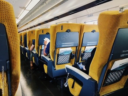 Comfortable Interior of a Modern Passenger Train with Bright Yellow Seats and Passengers Relaxing and Reading