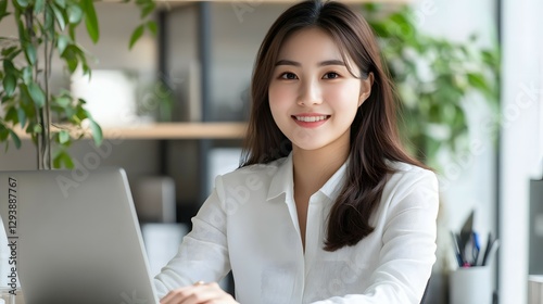 A smiling young beautiful businesswoman sitting at her desk with a laptop in a modern office