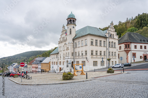 Fototapeta Naklejka Na Ścianę i Meble -  The Town Hall in Jachymov showcases its beautiful architecture against a backdrop of gray clouds. Visitors explore the square, enjoying the charming atmosphere of this historic site.