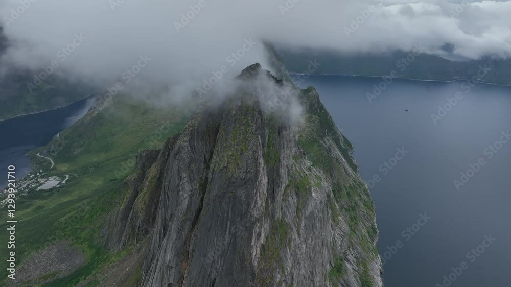 Drone footage of Segla rocky mountain and a lake behind clouds on Senja Island in Norway