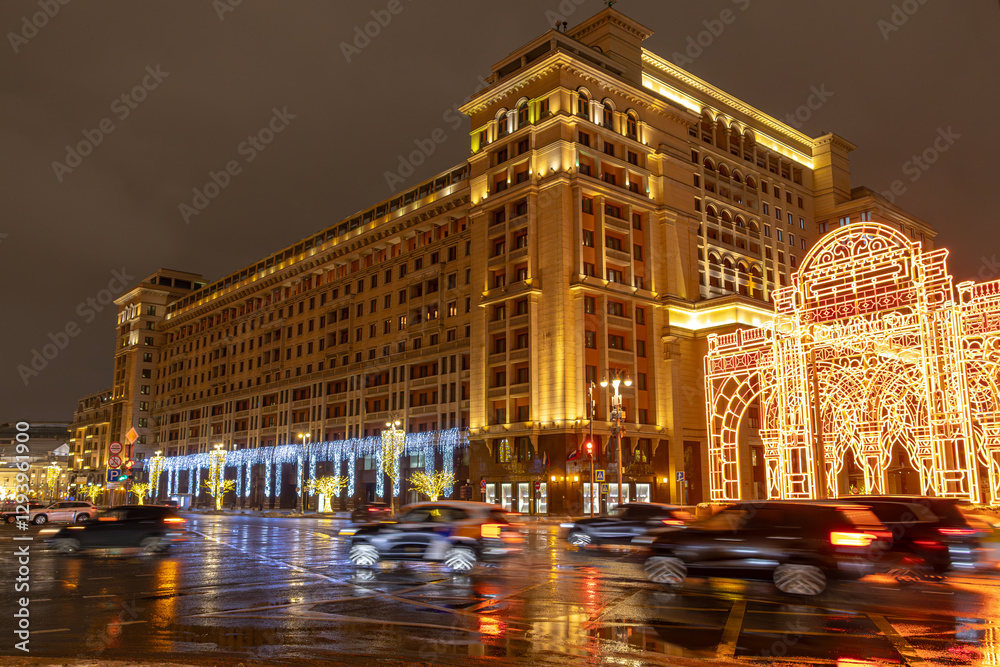 Naklejka premium A large historical building in Moscow with festive illumination at night. A city street at dusk with passing cars. Car traffic at night. Moscow at night.