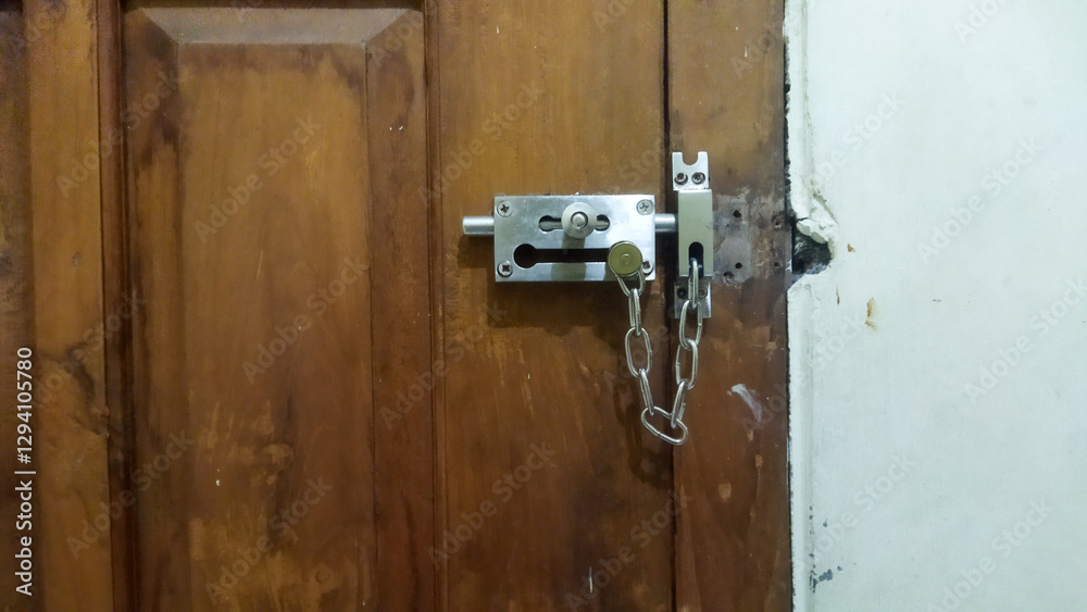 Secure metal door lock with a chain latch on a wooden door, symbolizing safety and protection inside a building. Secure metal door lock with a chain latch on a wooden door, symbolizing safety and protection inside a building.