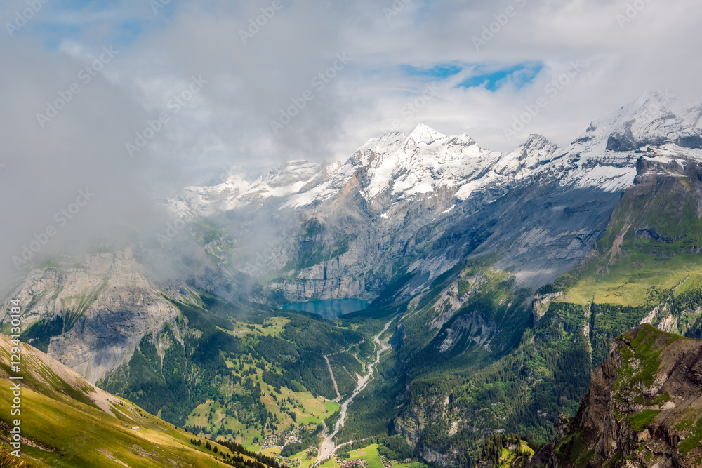 Naklejka premium Mixture of clouds with a mist over a picturesque alpine valley and blue mountain lake, Oeschinen Lake, Berner Oberland, Switzerland.