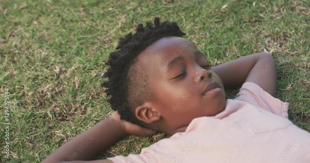 Lying on grass, African American boy relaxing with eyes closed, enjoying peaceful moment Lying on grass, African American boy relaxing with eyes closed, enjoying peaceful moment