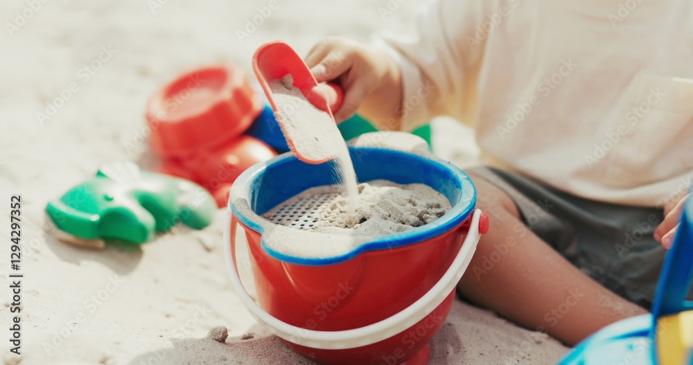 Boy plays in the sandbox, pouring sand from a shovel into a bucket, building castles on his own in the backyard.