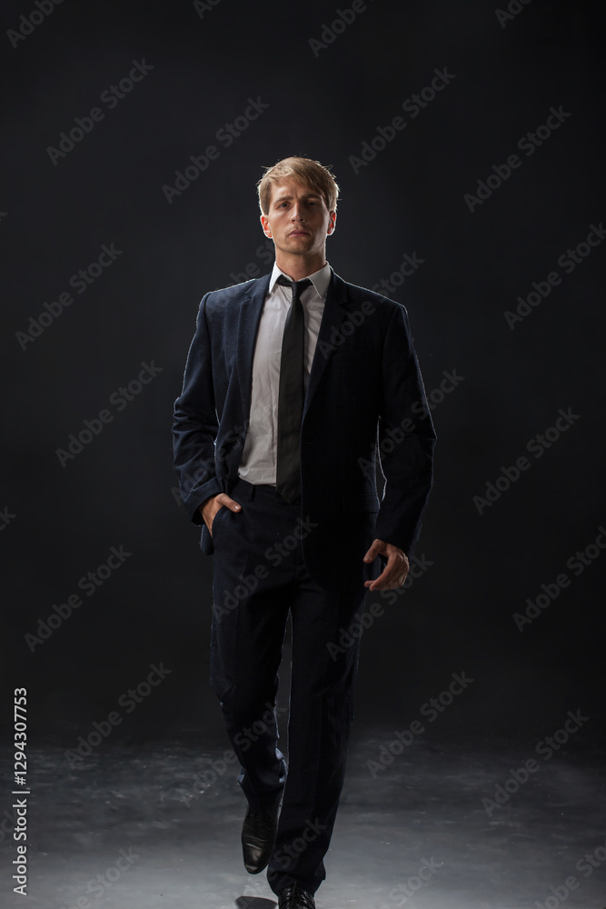 confident man strides forward in a dark suit, exuding authority and professionalism. The low-key, dark background highlights the formal attire in a corporate setting confident man strides forward in a dark suit, exuding authority and professionalism. The low-key, dark background highlights the formal attire in a corporate setting