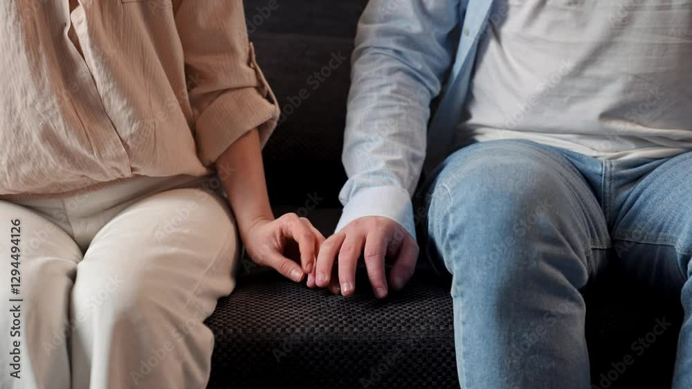 Lovely couple relaxing on the couch at home, close shot of man and woman sit on sofa and touching fingers and holding hands tight. Slow motion. Lovely couple relaxing on the couch at home, close shot of man and woman sit on sofa and touching fingers and holding hands tight. Slow motion.