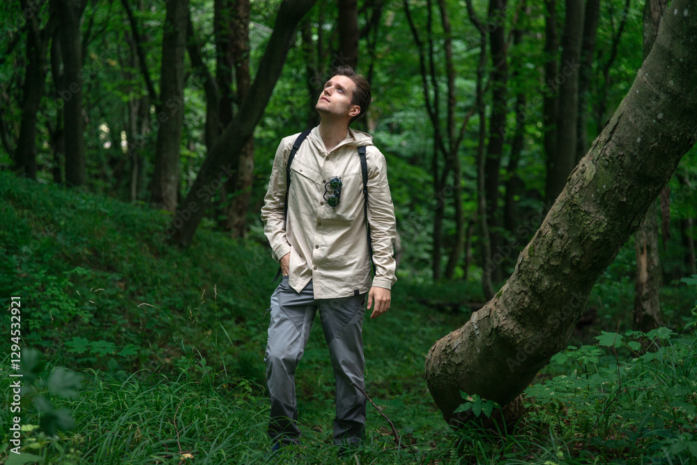 Adventurous man hiking in a forested mountain area, looking up. Sunlight filters through lush green trees. Adventurous man hiking in a forested mountain area, looking up. Sunlight filters through lush green trees.