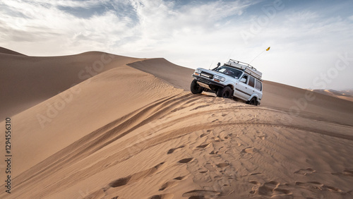 A 4x4 camper equipped with a roof tent crosses a sand dune of the Admer erg in the heart of the Algerian Sahara desert