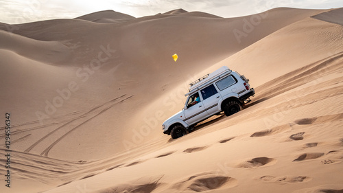 A 4x4 camper equipped with a roof tent crosses a sand dune of the Admer erg in the heart of the Algerian Sahara desert