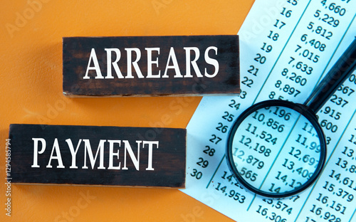 ARREARS PAYMENT - words on brown wooden bars against the background of a magnifying glass and a table with numbers