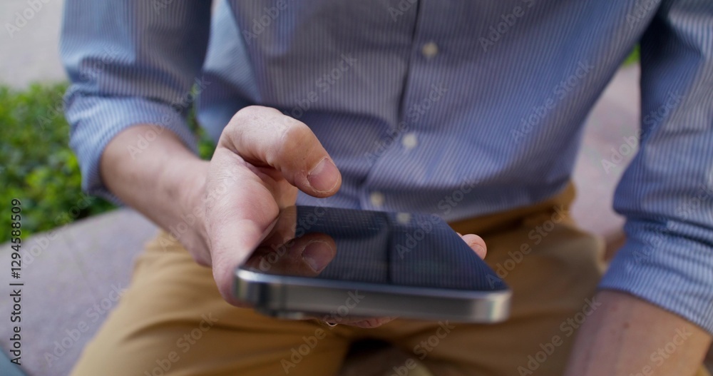 Fototapeta premium A man typing on a mobile phone in the city. Close-up of his hands. A businessman uses a smartphone