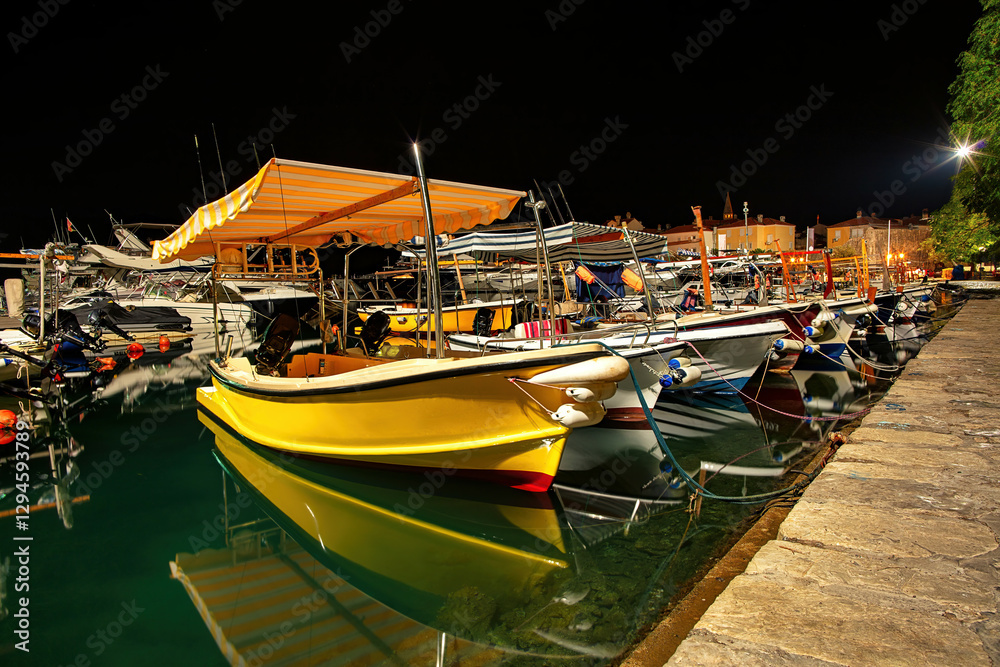 A peaceful night in Budva's lively harbor, filled with colorful boats and reflections.