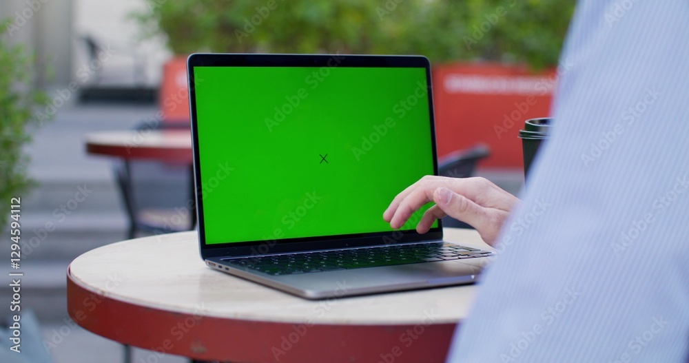A man typing on a laptop with green screen sitting at a table on a cafe terrace. Close-up of his hands, an unrecognizable person. Copy space A man typing on a laptop with green screen sitting at a table on a cafe terrace. Close-up of his hands, an unrecognizable person. Copy space
