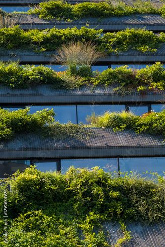 Close-up of a contemporary building with multiple layers of green rooftop terraces covered in diverse plants. Concept of sustainable architecture and urban garden greenery.