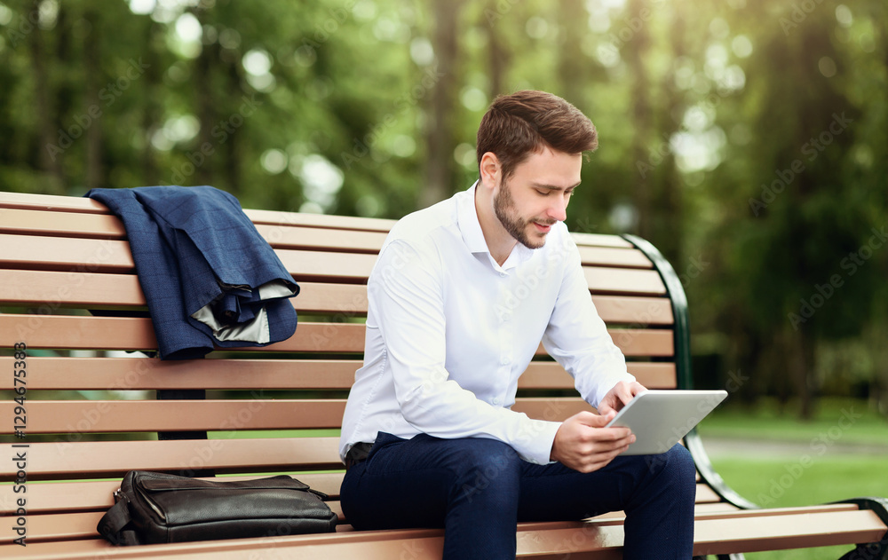 Handsome company employee relaxing on bench at park and browsing internet on tablet computer Handsome company employee relaxing on bench at park and browsing internet on tablet computer