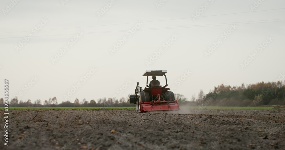 Obraz premium A young male farmer plows a field on a small farm tractor with a plow on an autumn day. Preparing the soil for planting winter crops
