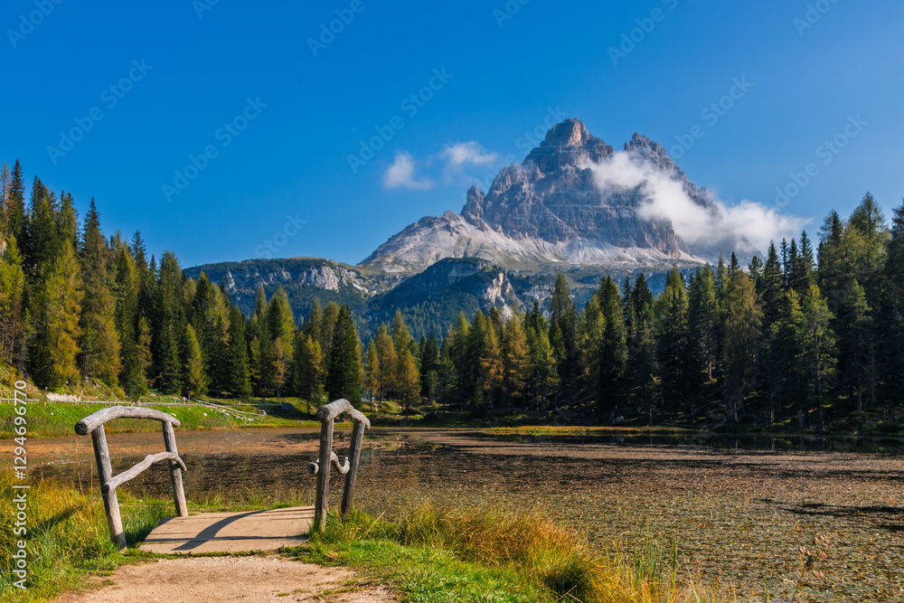 Tre Cime di Lavaredo during sunrise with warm golden light with small bridge and lake in the foreground